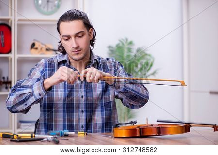 Young handsome repairman repairing violin