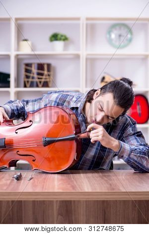 Young handsome repairman repairing cello