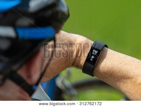 Beccles, Suffolk, England, Uk - July 20, 2019: Cyclist With Helmet Monitors Heart Rate On Fit Bit Ty