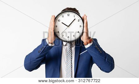Time Management Concept. Businessman Covering His Face With Clock On White Studio Background. Panora