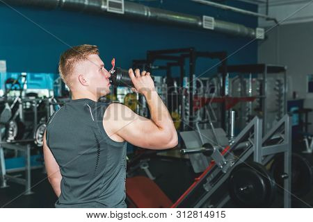 Athlete Drinking From A Shaker Botle For Sports Nutrition In The Background Of The Gym