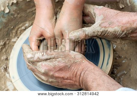 Two Pairs Of Hands Mold Something From Clay On A Potter's Wheel