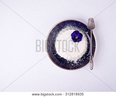 Panna Cotta Of White Cocolate And Wipped Cream Decorated Edible Violet Flower On Dark Blue Sauser Ov