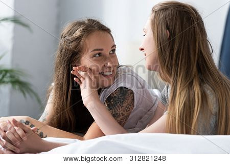 Two Lesbians Holding Hands And Looking At Each Other While Lying On Bed In Morning