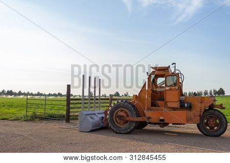 Side Angle Of Orange Tractor With A Plow In A Field With Blue Sky In The Background