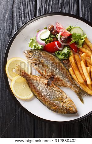 Portion Of Fried Salema Porgy Fish With Lemon, French Fries And Fresh Vegetable Salad Close-up On A