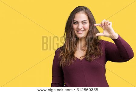 Beautiful and attractive plus size young woman wearing a dress over isolated background smiling and confident gesturing with hand doing size sign with fingers while looking and the camera.