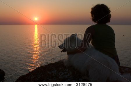 Pige og hund ser til solnedgang over et hav