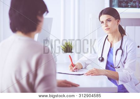 Doctor and patient discussing medical problems in a hospital consulting room. Doc filling in a patient's form