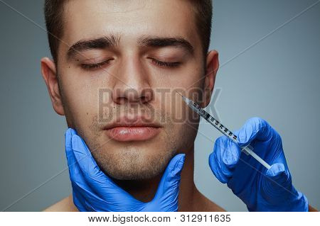 Close-up Portrait Of Young Man Isolated On Grey Studio Background. Filling Surgery Procedure. Concep