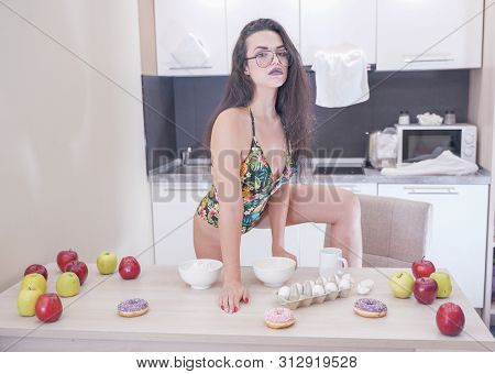 Happy Woman In Fashionable Swimsuit With Green Leaves Posing In White Kitchen