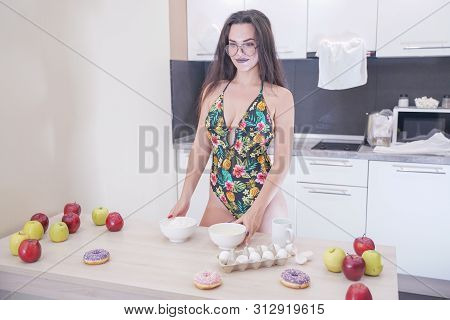 Happy Woman In Fashionable Swimsuit With Green Leaves Posing In White Kitchen