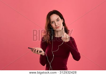 Portrait Of A Pretty Brunette Girl Holding Earphone In One Hand And Mobile Phone In Another One Expr