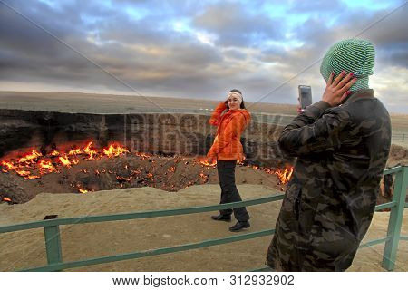 Turkmenistan, Darvaza - March 21, 2019: Girls Make A Photo On The Background Of The Burning Crater 