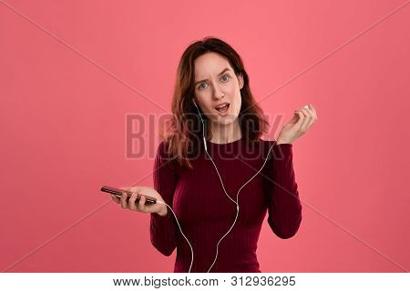 Portrait Of A Pretty Brunette Girl Holding Earphone In One Hand And Mobile Phone In Another One Expr