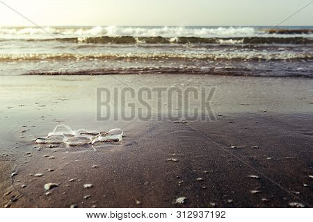 Background Of A Plastic Rings Lies On The Shore Of The Beach And Pollutes The Sea And The Marine Lif