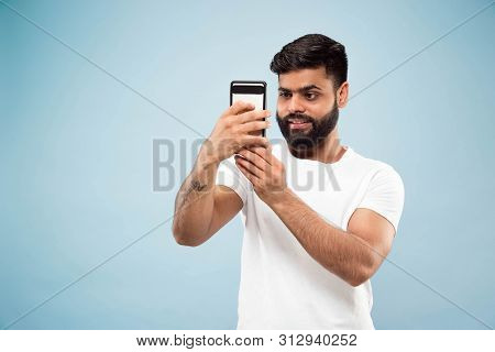 Half-length Close Up Portrait Of Young Hindoo Man In White Shirt On Blue Background. Human Emotions,