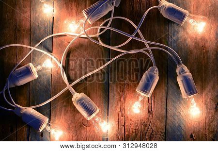 Electricity. Garland With Incandescent Lamps On A Wooden Background.