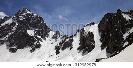 Panoramic View On Snow Covered Sunlit Mountain Range With Traces From Avalanches In Sunny Winter Day