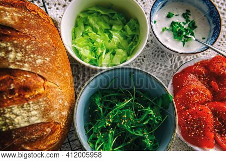 Vegetarian healthy breakfast containing homemade bread, vegetables tomatoes, argula with sesame seed, sald, iceberg lettuce and garlic sauce with chives