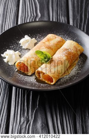 Delicious Crepes With Apricot Jam, Whipped Cream And Powdered Sugar Close-up In A Plate On The Table