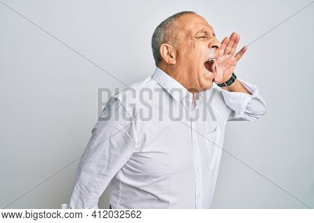 Handsome senior man wearing casual white shirt shouting and screaming loud to side with hand on mouth. communication concept. 