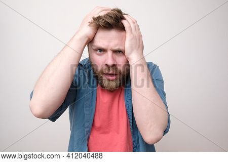 Man Is Stressed Or Has A Severe Headache, He Holds His Head With Hands And Looks At The Camera In Be