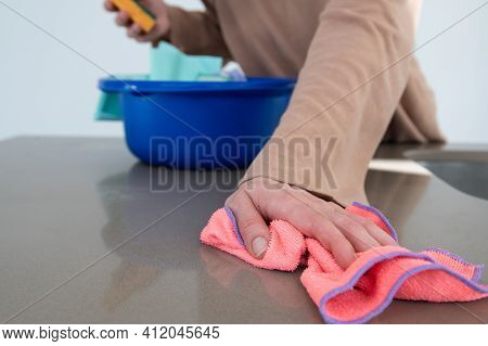 Woman's Hand Using A Colorful Rag To Wipe A Kitchen Counter Top.blue Bucket With Cleaning Rags In An