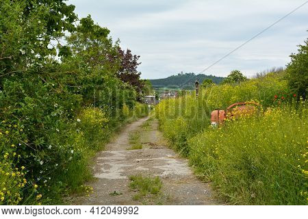 Path Between Meadow And Bushes With A View Of Ostheim, Bavaria, Germany With Old Cement Mixer In The