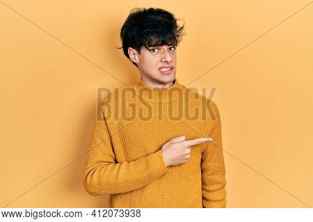 Handsome hipster young man wearing casual yellow sweater pointing aside worried and nervous with forefinger, concerned and surprised expression 
