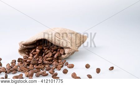 Falling Roasted Coffee Beans in jute bag. White background, close-up.