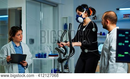 Doctor Witing On Clipboard Health Informations While Patient With Mask Running On Cross Trainer And 