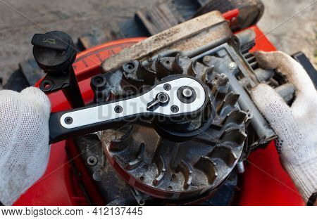 The Man Is Repairing The Mower In The Garage. He Tightens The Candle.