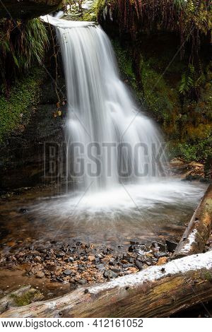 A waterfall cascades into a woodland glade in Maspie Den, Falkland, Fife during a winter morning
