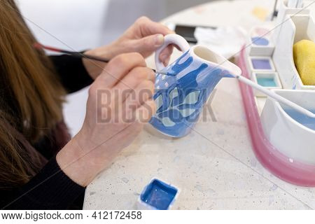 An Unrecognizable Female Ceramist Paints A Clay Milkman With A Brush. Ceramic Art Concept. Selective