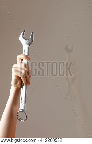 Big Spanner In The Woman's Hand. Hand Holds A Wrench On A Gray Background. Combination Wrench. Big C