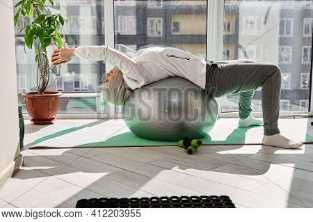 Arab Muslim Woman Wearing Headscarf And Sport Outfit Stretching Her Body On A Fitball Against The Ba