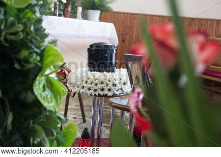 Black Urn On The Funeral Day In Church; Surrounded With Daisies And Roses