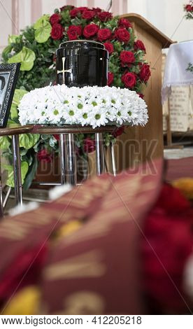 Black Urn On The Funeral Day In Church; Surrounded With Daisies And Roses