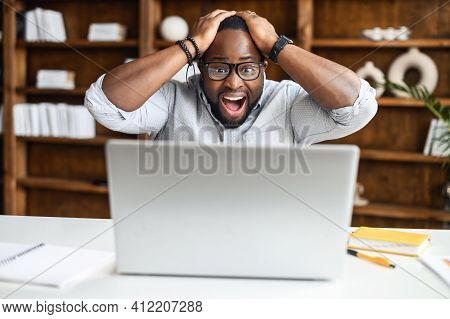 Shocked Man Is Staring On The Laptop Screen, Holding Head And Yelling Happily, Surprised African-ame
