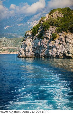 Wave Trace Tails Of Speed Boat On Blue Water Surface In The Sea. View On Grey Rock Islend