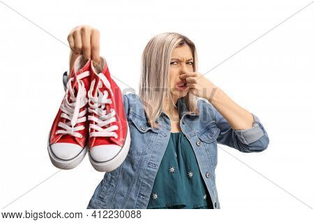 Young woman holding a pair of smelly sneakers isolated on white background