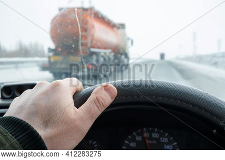 The Driver Hand On The Steering Wheel Of The Car, Which Is Overtaken On The Secondary Line By A Tank