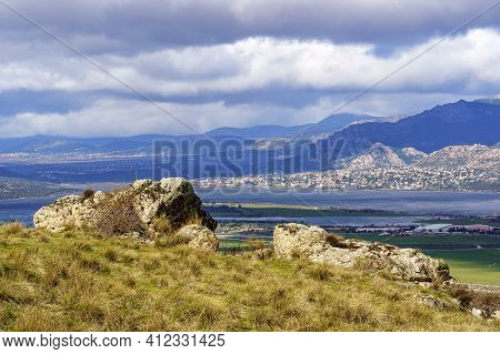 Green Landscape With Big Rocks, Lake And Mountains In The Background And White Clouds On Blue Sky. N