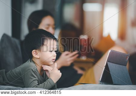 Asian Boy Looking At The Tablet Screen Attentively. Overstimulated Children Concept. Too Much Screen