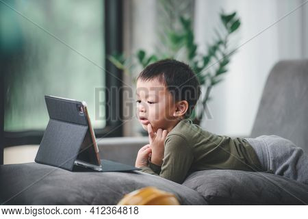 Asian Boy Looking At The Tablet Screen Attentively. Overstimulated Children Concept. Too Much Screen