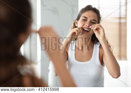 Woman Flossing Teeth With Tooth Floss Standing In Bathroom Indoor