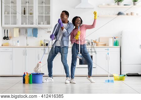 Cheerful Young Man And Woman Imitating Rock Stars While House-keeping