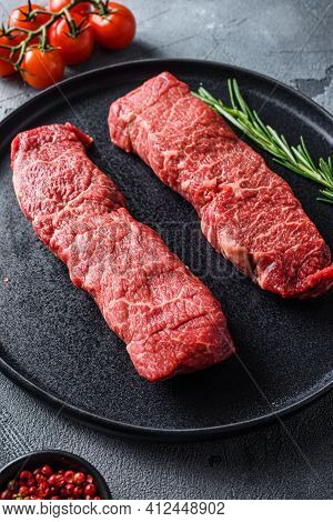 Organic Denver  Steak On Black Plate , Marbled Beef  With Herbs Tomatoes Peppercorns Over Grey Stone