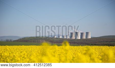 Nuclear Or Thermal Power Plant Chimneys With A Field Of Yellow Rapeseed In Front Of Them